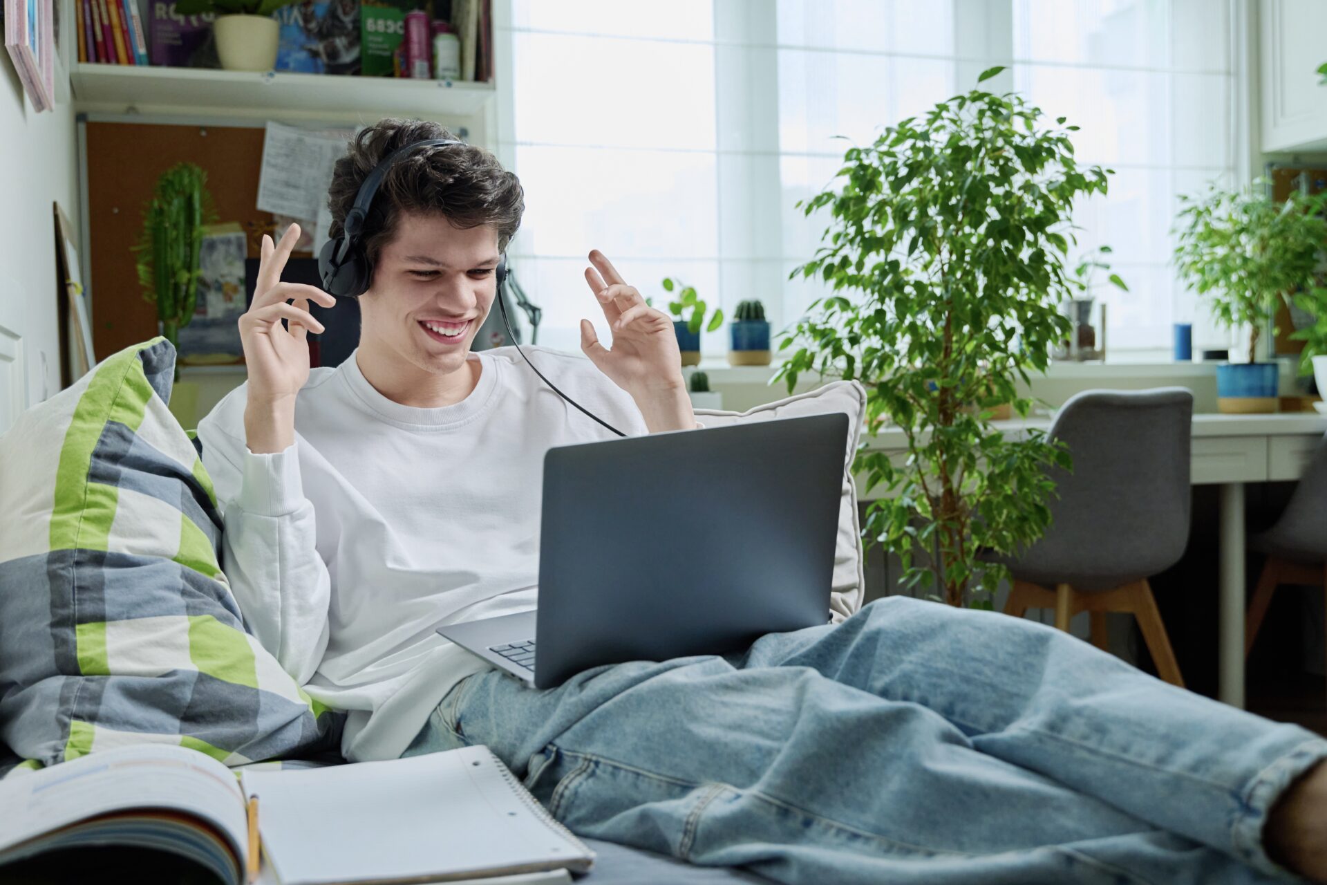 Young guy in headphones using laptop for video communication, lying at home