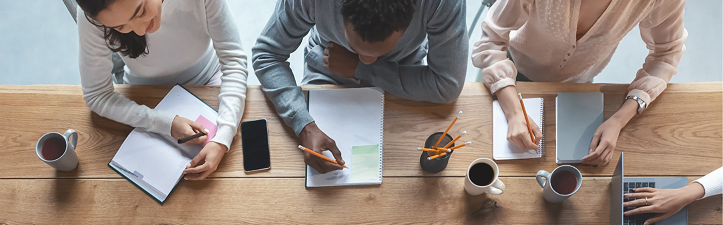an overhead shot of a meeting with multiple people taking notes and drinking coffee
